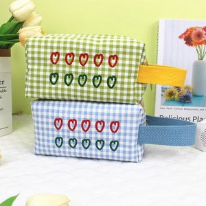 Detail of plaid makeup bags with heart embroidery and colorful woven handles