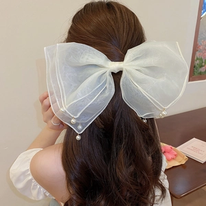 Detail of white mesh bow hair clip with pearl tassels worn by a model in soft light