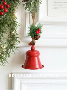 Détail d'une cloche de Noël en métal rouge mat avec pomme de pin et baies sur fond blanc