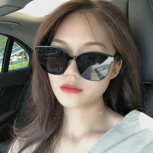 Asian woman wearing oversized black cat-eye sunglasses in a car with dark lenses