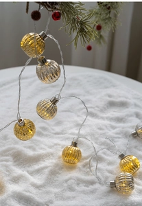 Detail of warm glow LED pumpkin ornaments on a festive snow-covered pine branch