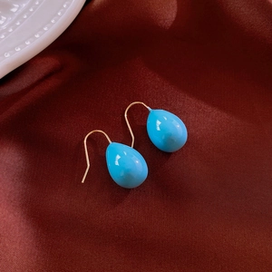 Macro shot of minimalist blue teardrop resin earrings on dark silk background