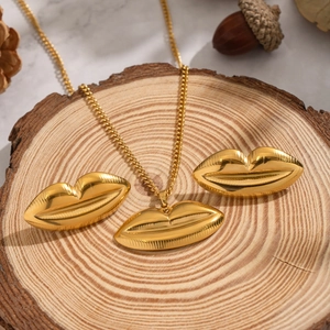 Golden lip pendant necklace and earrings set displayed on a rustic wood slice