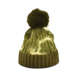 Close-up of olive green cable knit winter beanie with a large faux fur pompom detail