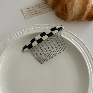 Detail view of a checkered acetate hair comb with sturdy metal teeth on a ceramic plate