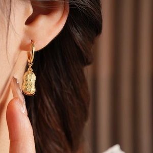 Close-up of gold-plated peanut-shaped hoop earrings with glass bead on model