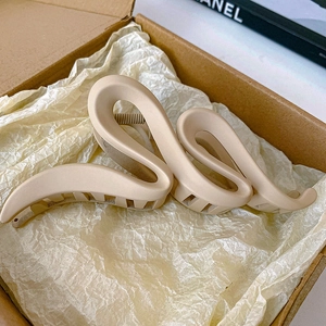 Detailed view of a beige snake-shaped hair claw clip inside a minimalist cardboard gift box