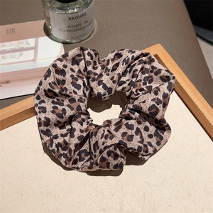 Detail of trendy leopard print fabric hair scrunchie placed on a minimalist wooden tray