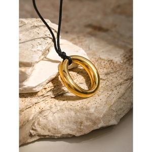 Detailed macro view of 18k gold-plated hollow circular pendant with black wax cord on a stone