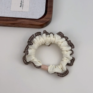 Close-up of cream scrunchie with brown checkered edges and a pink oval bead detail