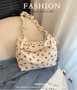 Corduroy strawberry print shoulder bag with a ruffled strap on a white sofa backdrop