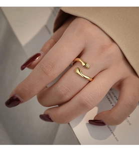 Detailed view of gold embrace hands open ring on finger against fashion magazine