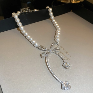 Détail du collier de perles avec pendentif en forme de nœud argenté et strass brillants