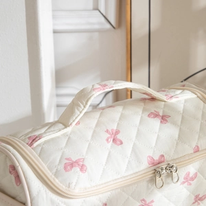 Close-up of quilted cream cosmetic bag with pink bows and double zipper detail