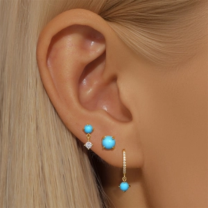 Macro detail of turquoise heart earrings and gold hoop set worn on model's ear