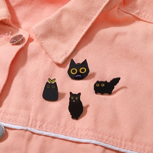 Set of four cute black cat enamel pins pinned on pink denim fabric for accessories