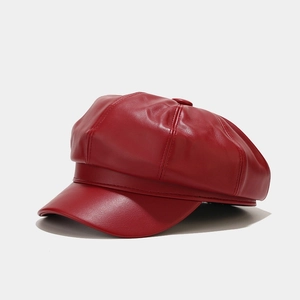 Detail of red faux leather newsboy cap with textured finish and decorative top button