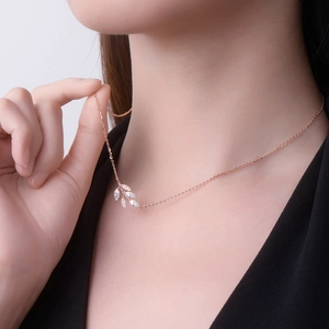 Rose gold leaf pendant necklace with D color moissanite stones shown on model neckline
