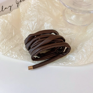 Detail of dark brown faux leather hair tie with elegant gold metal end caps on white paper