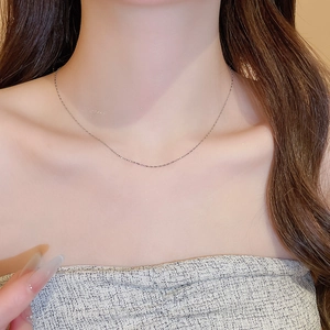 Close-up of minimalist stainless steel drop pendant necklace on a woman's neck