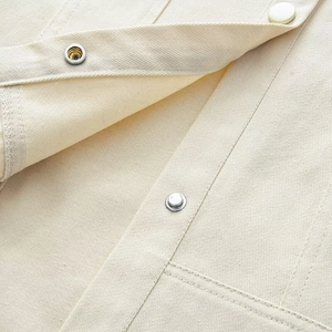 Detailed close-up of beige canvas jacket featuring reinforced stitching and silver metal snap buttons