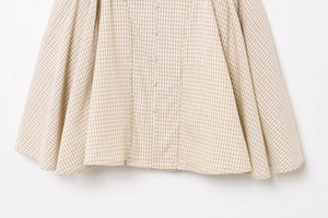 Detailed view of beige plaid dress hem with woven fabric buttons and fine texture