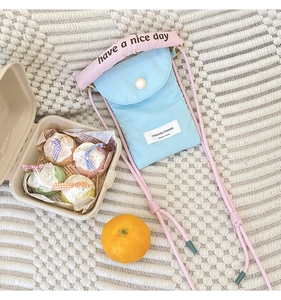 Detail of light blue fabric phone bag with pearl button and pink top handle text