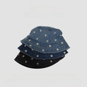 Close-up of stacked denim bucket hats featuring embroidered daisy patterns and stitched brims