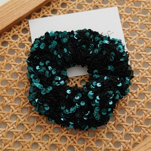 Close-up of dark green sequin scrunchie on a woven rattan surface with white card detail