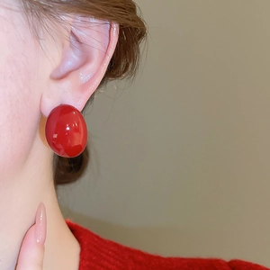 Close-up of model wearing large red oval stud earring with glossy enamel finish