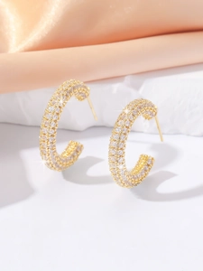 Detailed close-up of C-shaped gold earrings with paved white zircons on warm satin