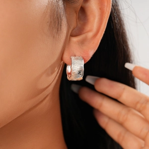 Close-up of silver-tone metal huggie earrings with a unique bark texture on the model