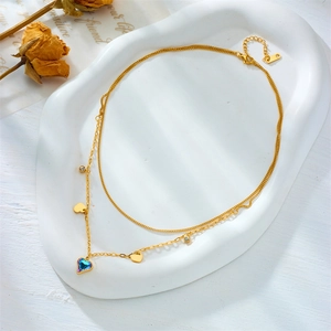 Close-up of double layer gold chain necklace featuring blue heart crystal and small charms