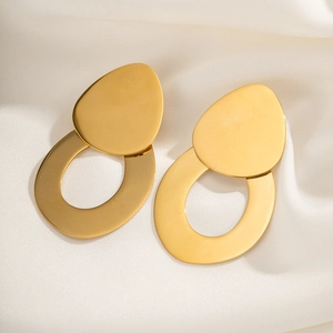 Close-up of golden teardrop and oval earrings on white silk fabric with soft lighting