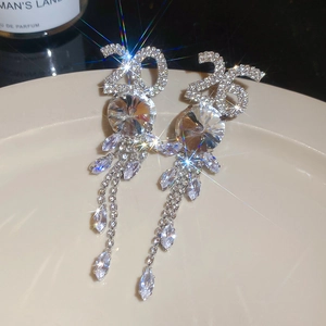 Détail de longues boucles d'oreilles à pompon argenté avec strass 2025 et zircon