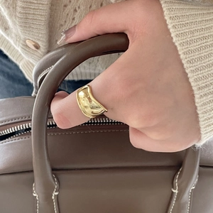 Golden wide wave ring with irregular lava texture worn by a model in a minimal setting