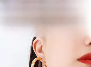 Detail of a model wearing chunky gold twisted hoop earrings in French luxury style