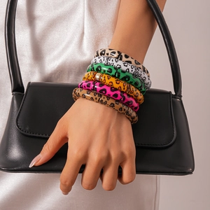 Detail shot of a stack of six colorful leopard print acrylic bangles on a model's wrist