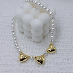 Elegant white pearl necklace featuring three polished golden heart charms on waffle fabric