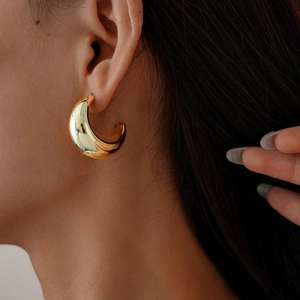 Macro view of gold crescent hoop earrings with a polished metallic finish on a model