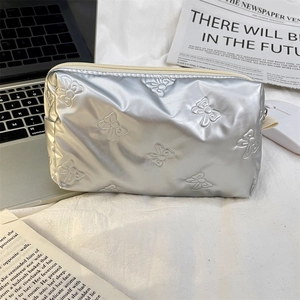 Detail of silver quilted makeup bag with embossed bow patterns and metal finish surface