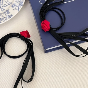 Detail of red fabric rose accessory on a long black silk ribbon bow for hair or neck
