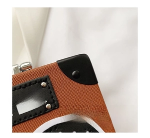 Detail view of brown cross-textured leather bag with BOOM POWER plate and rivets