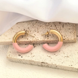 Detail view of gold and pink C-shaped earrings on beige travertine with silk fabric