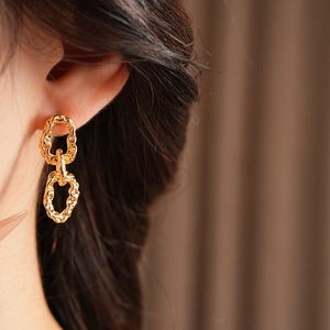 Gros plan de boucles d'oreilles dorées plissées avec texture irrégulière sur modèle