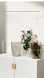 Minimalist transparent waste bin in grey and clear plastic on a white cabinet with roses