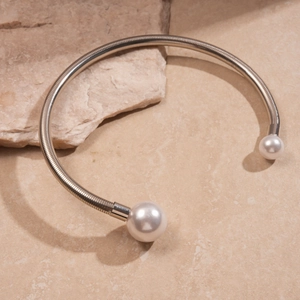 Detail of silver metallic choker featuring two large white pearls on a textured rock surface
