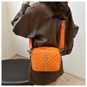 Orange quilted crossbody camera bag with gold SS logo and fringe shown on shoulder