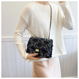 Close-up of black tweed chain bag with gold metal turn lock on elegant outfit