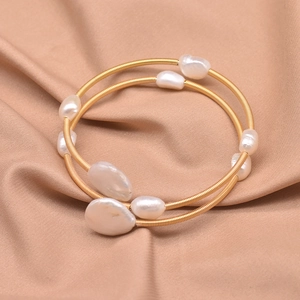 Macro shot of baroque pearls and gold-tone layered wire bracelet on satin fabric